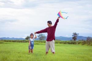 Aziatisch kindmeisje en vader met een vlieger die en gelukkig op weide in de zomer in de natuur rent foto