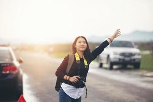 Aziatische jonge vrouwen die met rugzakken wandelen, gestrest na een autopech met een rode driehoek van een auto op de weg en een vrouw die met opgeheven armen langs de weg staat. foto