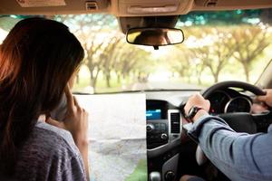 Aziatische man en vrouw die mobiel gebruiken op roadtrip en gelukkig jong stel met een kaart in de auto. wazig en zachte focus foto