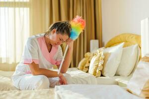 beeld van verdrietig overwerkt hotel hulp in de huishouding zittend Aan de bed in een kamer. foto