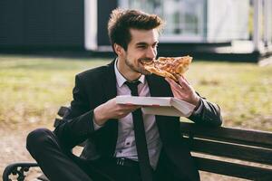 elegant zakenman geniet aan het eten pizza Aan zijn lunch breken terwijl zittend buiten.afgezwakt afbeelding. foto