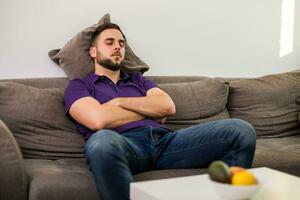 Mens viel in slaap terwijl terwijl zittend Aan sofa in zijn leven kamer. foto