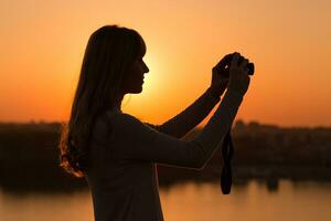 silhouet van een vrouw fotograferen Bij de zonsondergang. foto