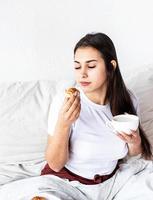 jonge brunette vrouw zittend in het bed met croissants eten foto