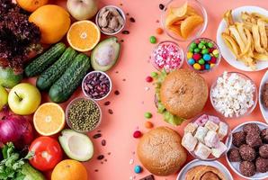 fruit en groenten versus snoep en fastfood bovenaanzicht plat op oranje achtergrond foto