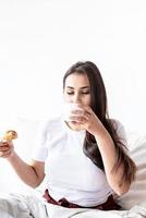 jonge brunette vrouw zittend in het bed met croissants eten foto