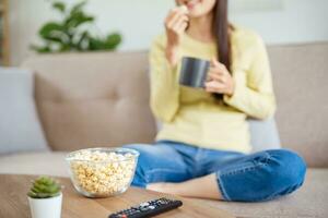 Aziatisch vrouw aan het kijken slim TV en gebruik makend van afgelegen controleur hand- Holding televisie audio afgelegen controle Bij huis met de afgelegen controle televisie foto