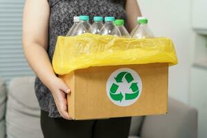 huis recycle eco groen nul concept vrouw het werpen leeg plastic fles in recycling bak met geel vuilnis Tassen Bij huis. foto