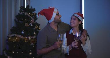 portret van jong Mens zijn omarmen hun vriendinnen, Holding een glas van wijn en genieten van staand naast de Kerstmis boom in de kamer, geliefden hebben moment romantisch en gelukkig samen foto