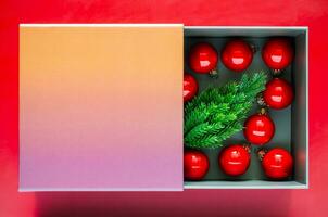 klein pijnboom boom en rood kerstballen in de doos dat hebben ruimte voor tekst Aan rood achtergrond. Kerstmis vakantie concept. foto
