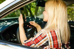 jong vrouw op zoek naar haar smartphone terwijl het rijden auto foto