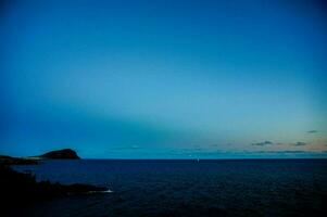 een blauw lucht over- de oceaan met een klein eiland in de afstand foto