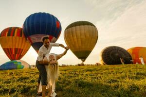 mooi romantisch paar knuffelen Bij weide. heet lucht ballon Aan een achtergrond foto