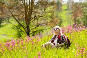 gelukkig avonturier vrouw staat Aan de groen berg helling tussen bloeiend roze rododendrons en op zoek in de afstand. episch reizen in de bergen. breed hoek. foto