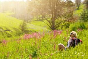 gelukkig avonturier vrouw staat Aan de groen berg helling tussen bloeiend roze rododendrons en op zoek in de afstand. episch reizen in de bergen. breed hoek. foto