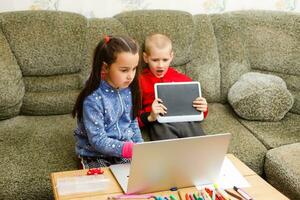afstand aan het leren online onderwijs. school- jongen en meisje aan het studeren Bij huis met laptop notitieboekje en aan het doen huiswerk. zittend Bij een tafel foto