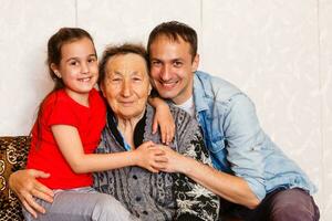 95 jaar oud vrouw en haar klein kleindochter kijken Bij de camera. ze is zittend Aan een stoel in haar leven kamer. foto