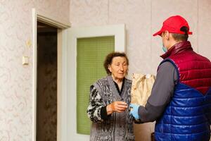 een ouderen vrouw blijft Bij huis. voedsel levering in een medisch masker naar de ouderen. foto