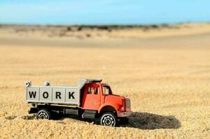 een speelgoed- vrachtauto met de woord werk Aan het is zittend in de zand foto
