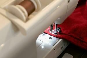 Mens gebruik makend van een naaien machine met een rood kledingstuk, voor reparatie werk, maatwerk, schepping, upcycling foto