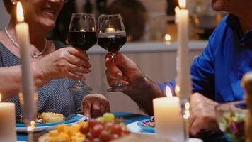 gelukkig vrolijk senior ouderen paar dining samen met rood wijn in de knus keuken. oud gepensioneerd oud mensen genieten van de maaltijd, vieren hun verjaardag in de dining kamer. foto