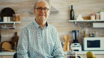 senior Mens in keuken glimlachen op zoek Bij camera Holding heet koffie beker. portret van ontspannen ouderen ouder persoon in de ochtend, genieten van vers warm drankje. gezond glimlachen volwassen gezicht foto