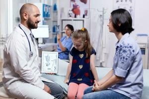 dokter Holding tablet pc met digitaal radiografie gedurende overleg van kind. gezondheidszorg arts specialist in geneeskunde het verstrekken van Gezondheid zorg Diensten behandeling inspectie. foto