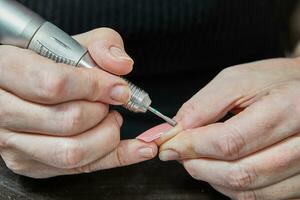 professioneel nagel technicus het uitvoeren van gel nagel uitbreiding en manicure gebruik makend van machine foto