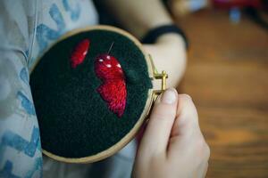 vrouw is borduren paddestoel pet Aan groen lap. meisje naaien floss met draden Bij huis Aan een houten kader. handgemaakt, ambacht, hobby. foto