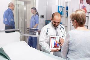 dokter uitleggen behandeling voor hart ziekte naar senior vrouw in overleg kamer. cardioloog vervelend stethoscoop bespreken met geduldig over ongezond hart ziekte. foto