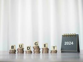 2024 bureau kalender en houten blokken met de woord begroting Aan stack van munten. de concept over begroting planning en toewijzing in jaar 2024 foto