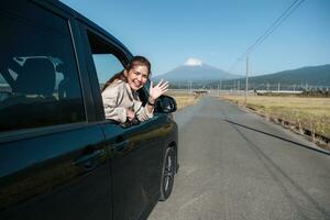 Aziatisch vrouw weg reis en vrijheid van auto venster voor voorjaar pauze, vakantie en buitenshuis avonturen in landelijk Japan in de omgeving van monteren fuji. portret van gelukkig jong vrouw het rijden Aan weg reis. foto