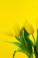 boeket van geel tulpen met groen bladeren Aan een geel achtergrond. verticaal. gelukkig Internationale vrouwen , moeder en Valentijnsdag dag, verjaardag, vakantie. kopiëren ruimte foto