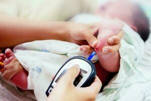 handen van pediatrisch verpleegster houden en gebruik makend van bloed en glucose meter met vel controleren tintje Aan ziek pasgeboren baby bloed en foots naar controle glucose in zijn bloed Bij nicu afdelingen. foto