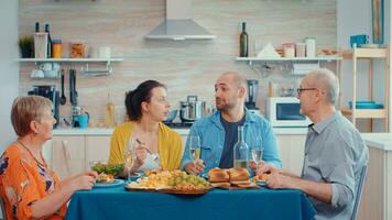 uitgebreid familie pratend hebben ontspannende tijd. multi generatie genieten van tijd Bij huis, in de keuken zittend door de tafel, aan het eten avondeten samen en drinken foto