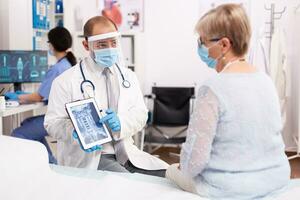 9ziekenhuis specialist met gezicht masker bespreken digitaal röntgenstraal Holding tablet pc in de Cursus van covid pandemie. medisch arts specialist gedurende coronavirus het uitbreken bespreken met geduldig. foto