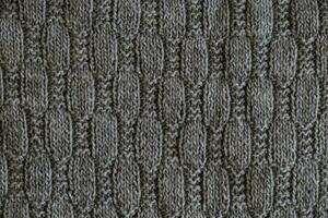 structuur van glad gebreid grijs trui met patroon. top visie, detailopname. handgemaakt breiwerk wol of katoen kleding stof textuur. achtergrond met gebreid blad vorm geven aan, breiwerk patroon met kabels. foto