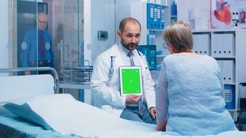 dokter Holding een groen scherm tablet met geïsoleerd mock-up in voorkant van ouderen geduldig in een privaat modern ziekenhuis of kliniek. klaar chroma mockup voor uw app, tekst, video of andere digitaal Bedrijfsmiddel foto