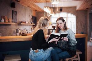 twee meisjes verzonken in leesboek tijdens de pauze in café. schattige mooie jonge vrouwen lezen een boek en drinken koffie foto