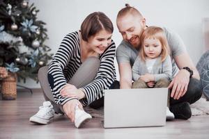 jong gezin van drie met laptop terwijl ze thuis op tapijt liggen foto