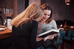 twee meisjes verzonken in leesboek tijdens de pauze in café. schattige mooie jonge vrouwen lezen een boek en drinken koffie foto