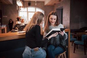 twee meisjes verzonken in leesboek tijdens de pauze in café. schattige mooie jonge vrouwen lezen een boek en drinken koffie foto