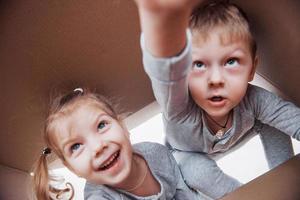 twee kleine jongens en meisjes die een kartonnen doos openen en er middenin klimmen. kinderen hebben plezier foto