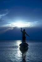 silhouetten van visser Bij de meer met zonsondergang, Thailand. foto