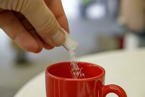 hand- zetten suiker in een kop van koffie of thee. dichtbij foto