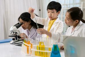 kind jongen in wit japon aan het doen een chemisch experiment in laboratorium Bij school- met leraar door dropping reagens in test buis. foto