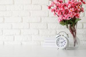 witte retro wekker op witte bakstenen muur met boeken en bloemen met kopieerruimte foto