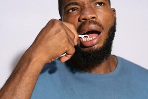 jong zwart Mens gebruik makend van een floss naar schoon zijn tanden foto