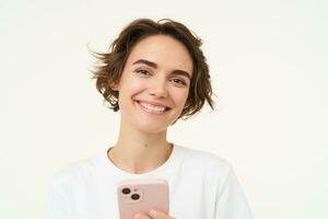 portret van jong vrouw staand met roze mobiel telefoon, gebruik makend van smartphone app, aan het doen online winkelen, betalen voor iets gebruik makend van sollicitatie, staand over- wit achtergrond foto