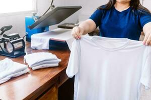 onherkenbaar vrouw, Holding wit overhemden achter een sublimatie of scherm het drukken machine voor t-shirts. foto